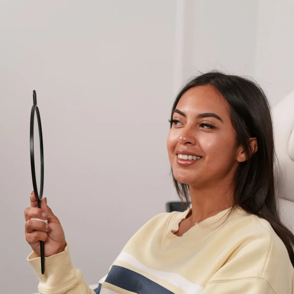 A patient smiling at her new smile in a hand mirror